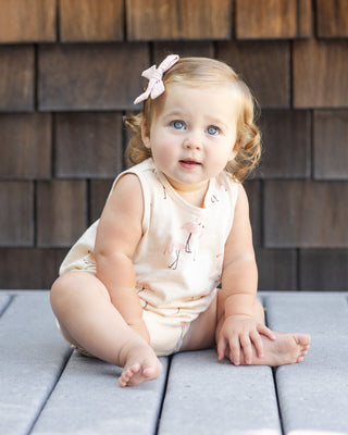 Rylee & Cru Bubble Romper - Flamingo
Baby sitting on a wooden deck wearing a light-colored outfit with a pink bow in hair.