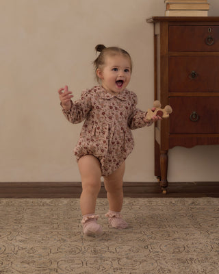 Rylee & Cru Cora Romper - Pink Floral
A toddler girl wearing a long-sleeve floral romper and pink booties is walking and smiling in a room with a wooden dresser and patterned rug.