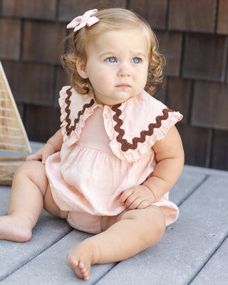 Rylee & Cru Cove Romper - Blush
Baby wearing a pink outfit with ruffled collar sitting on a wooden deck.