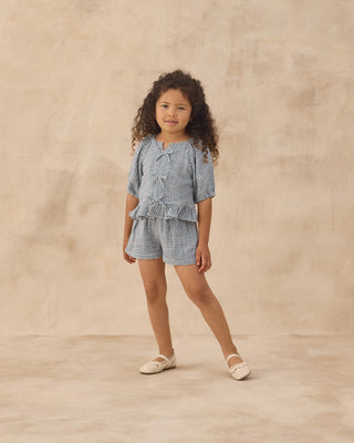 Rylee & Cru Juniper Set - Marine Gingham
Young girl wearing a blue checkered outfit on a beige background