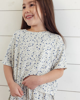 Rylee & Cru Mosie Set - Blue Ditsy
Young girl wearing a floral dress against a white wooden background