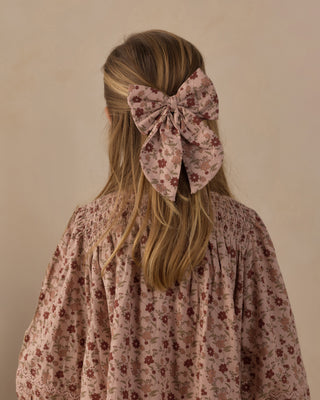 Rylee & Cru Oversized Bow - Pink Floral A blonde girl viewed from behind, wearing a large dusty pink floral hair bow accessory in her hair, paired with a matching smocked blouse.