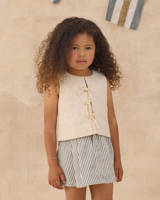 Rylee & Cru Pleated Denim Skirt - Railroad Stripe
Young girl wearing a sleeveless top and striped shorts against a beige wall.