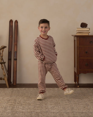 Rylee & Cru Relaxed Set - Brick Stripe
A young boy wearing a two-piece pajama set with brown and beige horizontal stripes, standing in a cozy room with a wooden dresser, vintage skis, and a patterned rug.