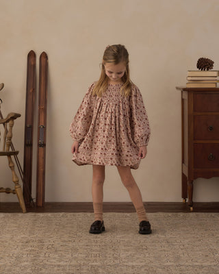 Rylee & Cru Selene Dress - Pink Floral
A young girl stands in a vintage-style room wearing a dusty rose pink smocked blouse with a small floral print, paired with beige socks and black shoes.