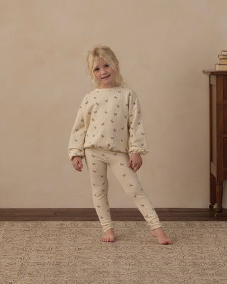 Rylee & Cru Spongy Knit Set - Butterfly Ditsy
A young blonde girl stands barefoot indoors wearing a cream-colored two-piece pajama set with a small repeating gray pattern. The set includes a long-sleeve top and matching pants.