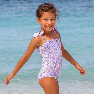 Shade Critters Girls Smocked One Piece Swimsuit - Wildflower Fields
Young girl in a floral swimsuit standing on a beach with clear blue water.