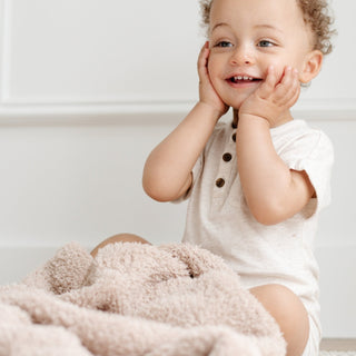 Saranoni Bamboni® Receiving Blanket - Birch
Child sitting on a soft surface with a plush toy, wearing a white shirt.