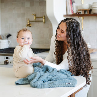 Saranoni Bamboni® Receiving Blanket - Spruce
Woman and baby in a kitchen setting with a blue blanket on a counter.