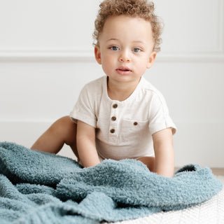 Saranoni Bamboni® Receiving Blanket - Spruce
Child sitting on a bed with a blue blanket