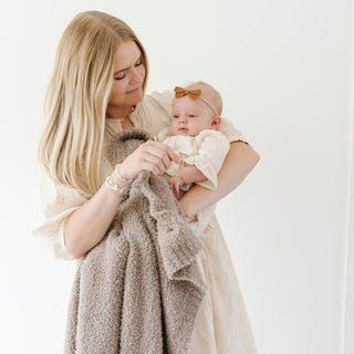Saranoni Bamboni® Receiving Blanket - Taupe
Woman holding a baby wrapped in a brown blanket against a white background