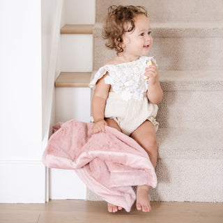 Saranoni Lush Mini Blanket - Ballet Slipper
Baby in a white outfit holding a pink blanket on a staircase