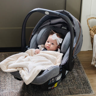 Saranoni Lush Mini Blanket - Natural
Baby in a car seat with a white blanket and bow, sitting on a rug.