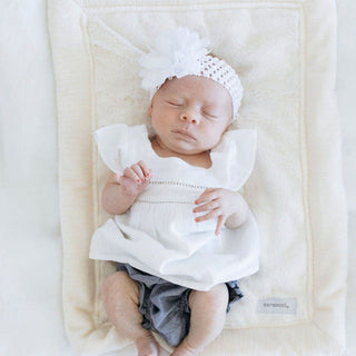Saranoni Lush Mini Blanket - Natural
Newborn baby wearing a white outfit and headband, lying on a textured blanket.