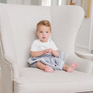 Saranoni Lush Mini Blanket - Storm Cloud
Child sitting on a light gray armchair holding a blue blanket