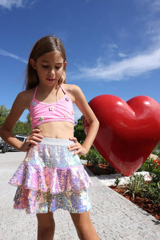 Lola and The Boys Sequin Ombre Ruffle Skirt
Young girl in a pink top and iridescent skirt standing next to a large red heart-shaped balloon outdoors.