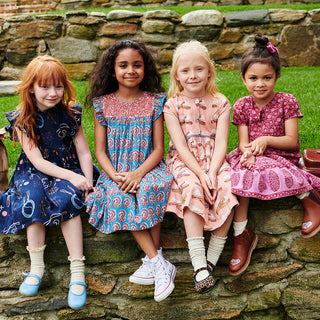 Pink Chicken Girls Fiona Ruffle Dress - Blue Paisley Four young girls sitting on a stone wall wearing patterned dresses.