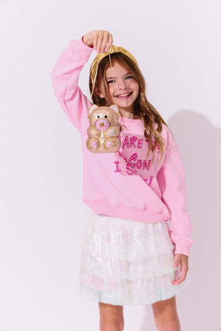 Lola and The Boys Snow Shimmer Tinsel Party Skirt
Young girl wearing a pink sweatshirt with a teddy bear graphic and text, holding a gold headband.