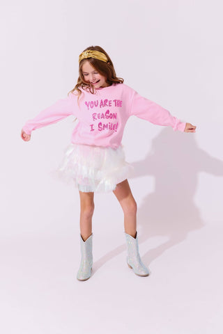 Lola and The Boys Snow Shimmer Tinsel Party Skirt
Person wearing a pink sweatshirt with text, white skirt, and gray socks on a light background