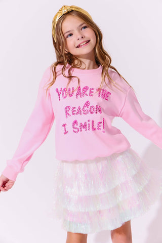 Lola and The Boys Snow Shimmer Tinsel Party Skirt
Young girl wearing a pink sweatshirt with text and a white skirt on a light pink background