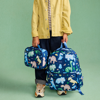State Bags Kane Backpack - Dino Fossils 
Person holding a blue backpack and lunch bag with dinosaur pattern on a green background