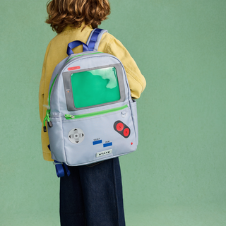 State Bags Kane Backpack - Vidoegame
A child wearing a yellow shirt and dark pants is shown from behind, carrying a light blue backpack designed to look like a retro video game console with a green screen, green zipper trim, and red buttons. The background is a solid sage green studio backdrop.