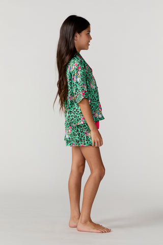 Sunshine Society Kids Silky Short Sleeve Short Set - Gilded Leopard
A young girl with long dark hair stands in profile against a light gray studio background, wearing a green short-sleeve kaftan-style cover-up with a pink and black animal print and a small pink bikini top.