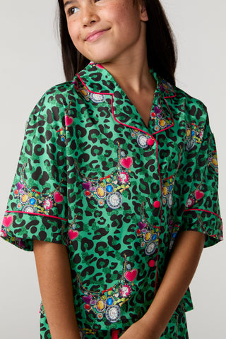 Sunshine Society Kids Silky Short Sleeve Short Set - Gilded Leopard
A young girl wearing a green short-sleeve pajama top with a black leopard print and colorful bicycle-themed graphics, shown against a plain light gray background.