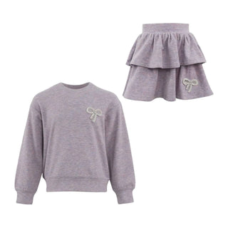 Lola and the Boys Super Soft Pearl Bow Set - Lavender
A children's two-piece outfit set in heathered light purple, featuring a long-sleeve crewneck sweatshirt and a matching tiered ruffle mini skirt, both with a small bow embellishment on the chest and hip.