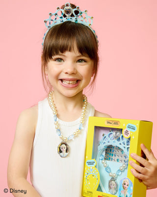 Super Smalls Disney Frozen Headband & Jewelry Kit
A young girl smiling and holding a Disney Frozen toy set box, wearing a light blue tiara and a pearl necklace with an Elsa pendant, against a solid pink background.