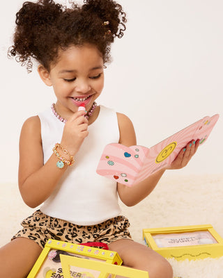 Super Smalls Mom's Beauty Starter Kit
Young girl playing with a pink toy, smiling, on a light background