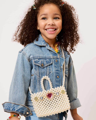 Super Smalls Pearl of the Party Handbag
Child wearing a denim jacket holding a decorative white handbag with a heart charm on a light background
