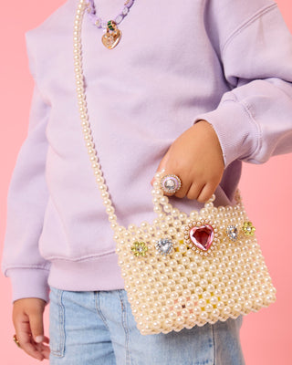 Super Smalls Pearl of the Party Handbag
Person holding a pearl-handled handbag with decorative elements against a pink background