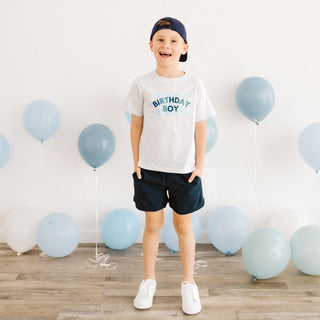 Sweet Wink Birthday Boy Checker Short Sleeve T-Shirt - Ash
Child wearing a 'Birthday Boy' shirt surrounded by balloons indoors.