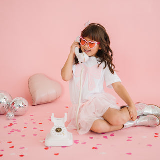 Sweet Wink Bow Lace Tiered Tutu
Young girl in a white dress with pink sunglasses on a pink background
