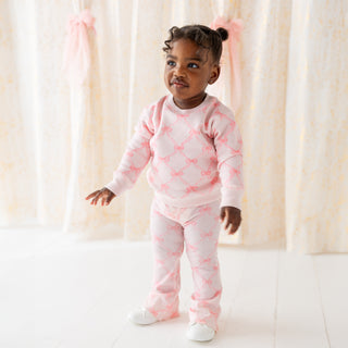 Sweet Wink Bow Trellis Sweatshirt & Flare Legging Set 
Child wearing a pink outfit with bow pattern against a light curtain background