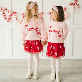 Sweet Wink Coquette Merry Christmas Knit Sweater
Sweet Wink Candy Cane Coquette Sequin Christmas Tutu
Two children wearing matching outfits with 'Merry' text and red skirts, standing against a white wall with decorative bows.