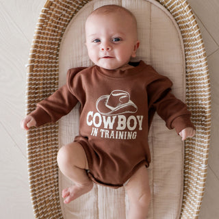 Sweet Wink Cowboy In Training Western Long Sleeve Romper
Baby wearing a brown 'Cowboy in Training' outfit lying on a woven mat.
