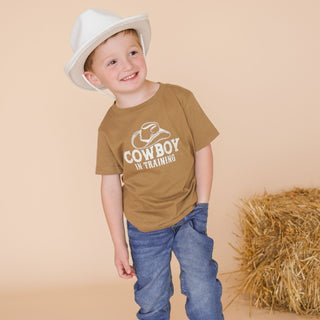Sweet Wink Cowboy In Training Western Short Sleeve T-Shirt
Child wearing a brown 'Cowboy in Training' shirt and white cowboy hat, standing next to a hay bale on a beige background.