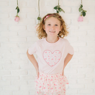 Sweet Wink Dainty Rose Pearl Heart Patch Short Sleeve T-Shirt - Ballet
Young girl wearing a pink heart-themed shirt and skirt against a white background with floral decorations.