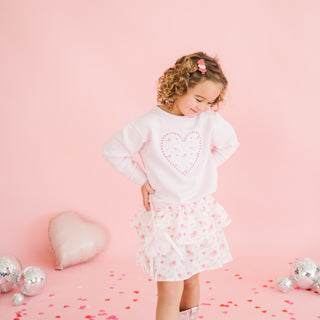 Sweet Wink Dainty Rose Skort
Young girl in a white dress with a pink heart design on a pink background