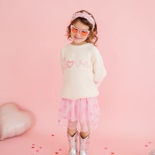 Sweet Wink Ditsy Love Valentine's Day Knit Sweater
Child wearing a cream sweater with pink heart designs, pink skirt, and sunglasses on a pink background.
