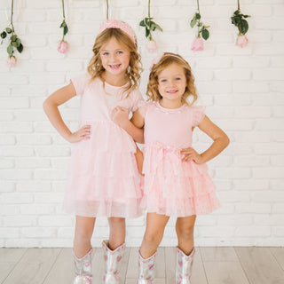 Sweet Wink Flocked Heart Valentine's Day Tiered Short Sleeve Tutu Dress
Two young girls in matching pink dresses standing against a white brick wall with floral decorations.