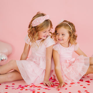 Sweet Wink Flocked Heart Valentine's Day Tiered Short Sleeve Tutu Dress
Two young girls in pink dresses sitting on a pink surface with heart patterns.