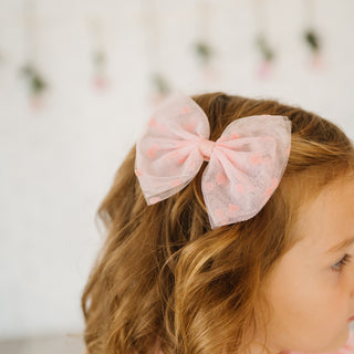 Sweet Wink Flocked Heart Valentine's Day Tulle Bow Clip
Child wearing a pink bow in their hair with a blurred floral background