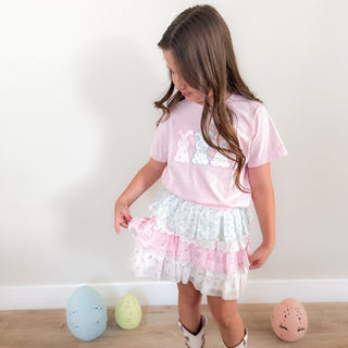Sweet Wink Floral & Lace Tiered Tutu
Sweet Wink Floral Bunny Patch Easter Short Sleeve T-Shirt - Ballet
Young girl wearing a pink top and white skirt with ruffles, standing on a wooden floor.