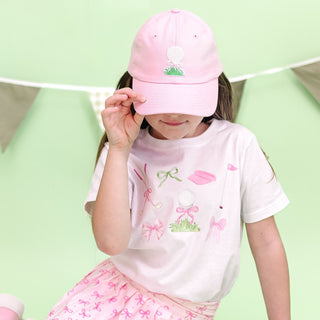 White Sweet Wink golf icon short sleeve T-shirt with a small logo patch, styled on a model alongside golf accessories.
