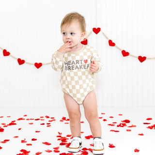 Sweet Wink Heartbreaker Checkered Valentine's Day Long Sleeve Romper - Natural
Baby wearing a 'Heart Breaker' onesie with red heart decorations on a white background