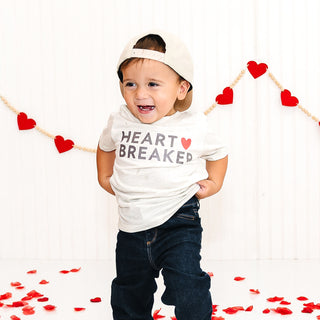 Sweet Wink Heartbreaker Valentine's Day Short Sleeve T-Shirt - Natural Heather
Child wearing a 'Heart Breaker' shirt with red heart decorations in the background