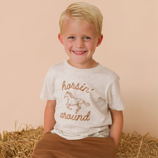 Sweet Wink Horsin' Around Western Short Sleeve T-Shirt
Child wearing a t-shirt with 'horsin' around' text and a horse graphic, sitting on hay.